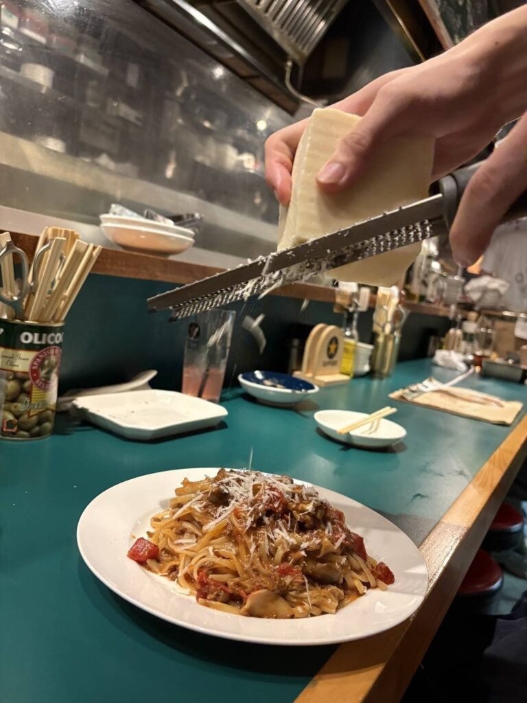 大衆イタリアンうめぼしの自家製ボロネーゼ。平打ち麺にチーズを削ってくれているところ