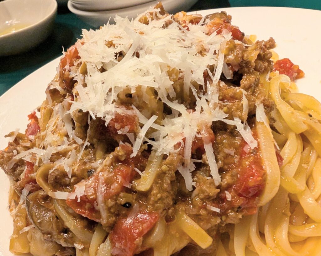大衆イタリアンうめぼしの自家製ボロネーゼ。平打ち麺に削りたてチーズをかけた状態