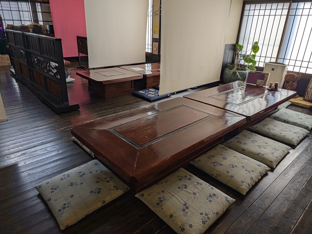 魚屋さんの台所の板張りに座卓と座布団が並ぶ座敷席